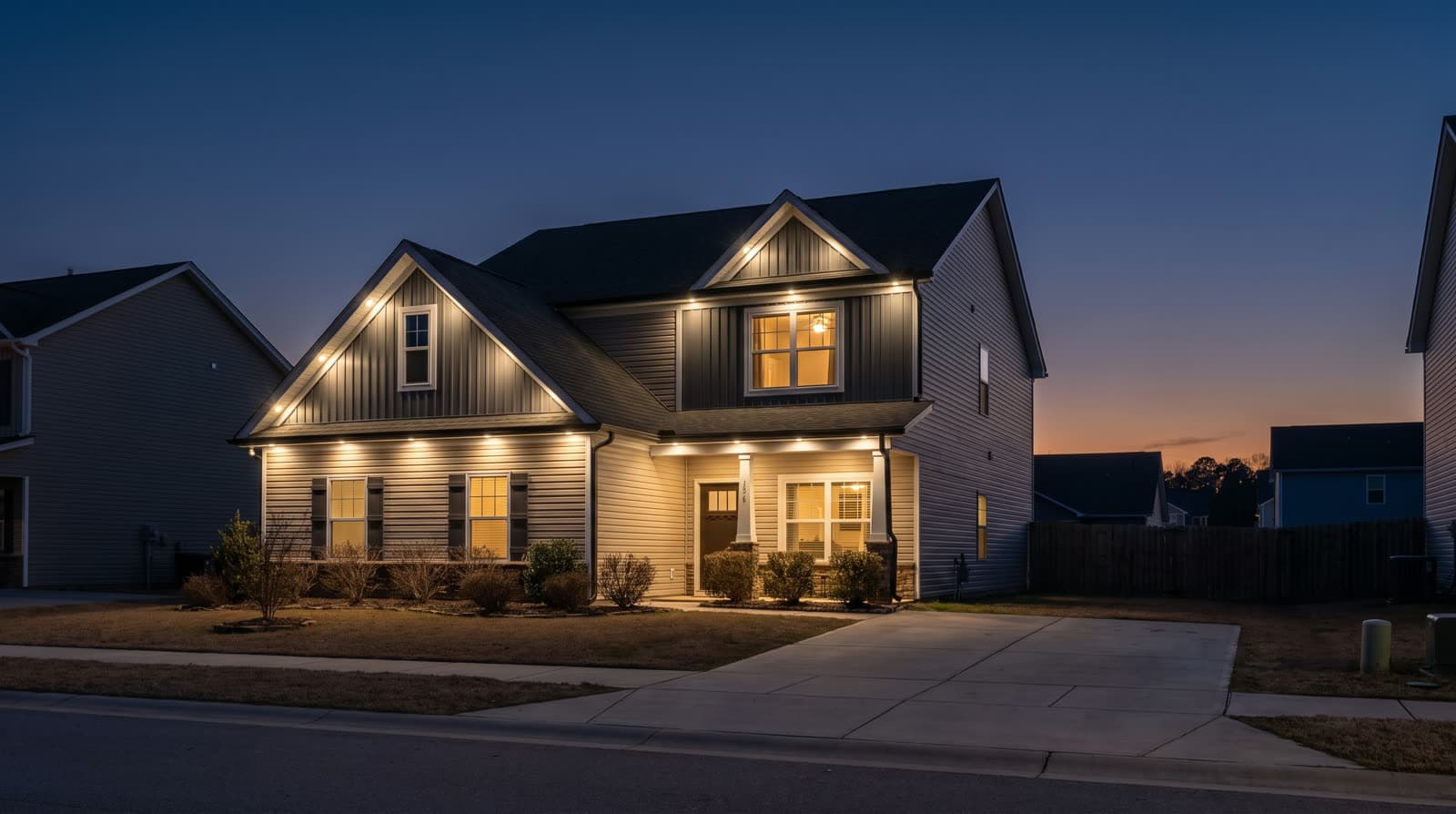 Two-story gray siding house with dark roof at blue hour, warm white lighting along the gable peaks and eaves
