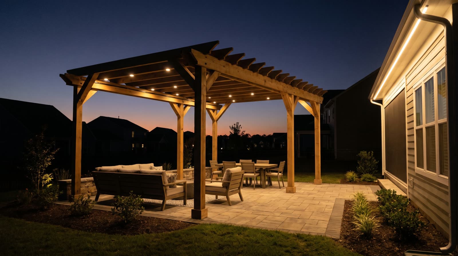 Wooden pergola at twilight with warm white lights recessed into the crossbeams over a paver patio with dining and lounge seating