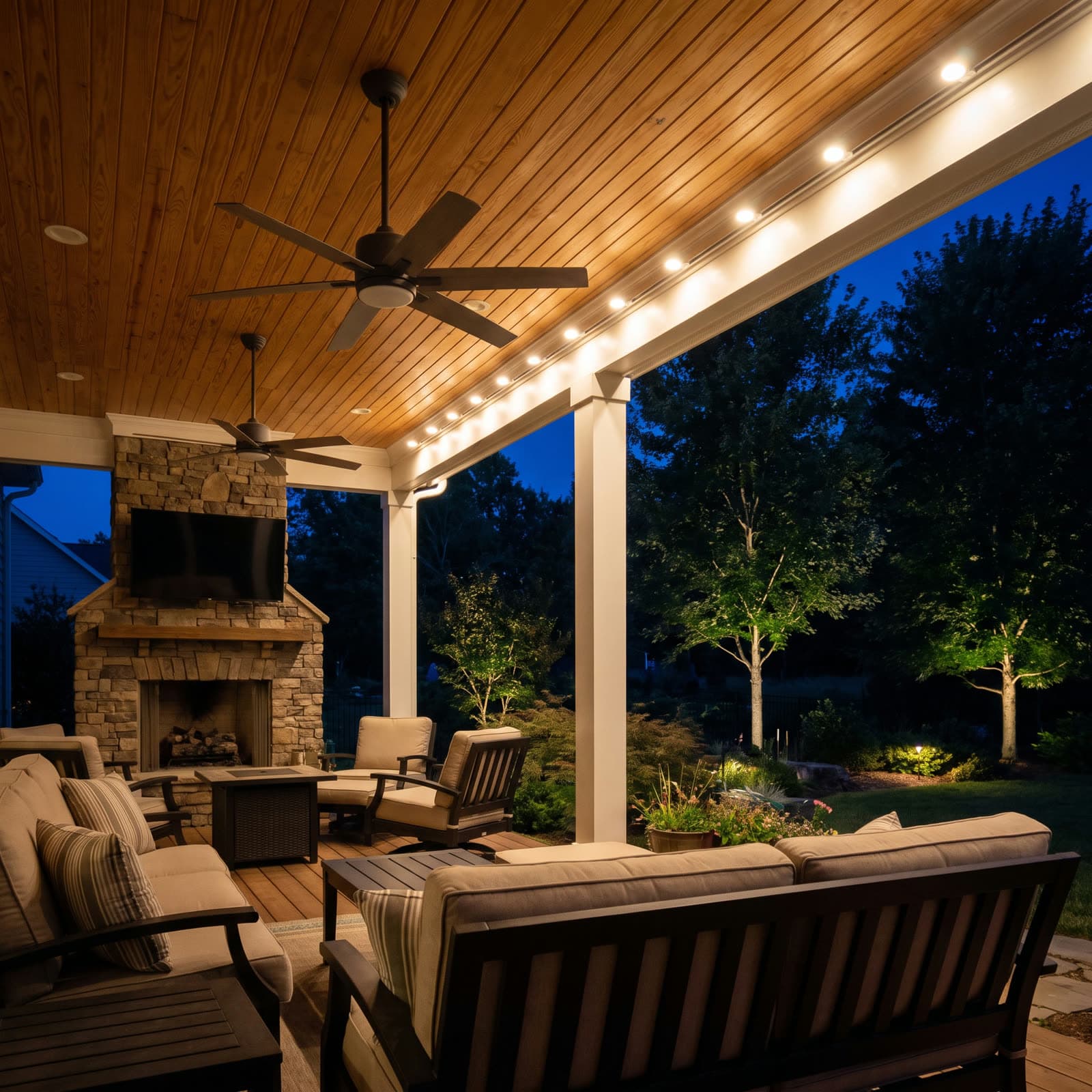 Covered outdoor porch ceiling at night with a warm white LED strip mounted along the fascia beam above a stone fireplace and lounge seating